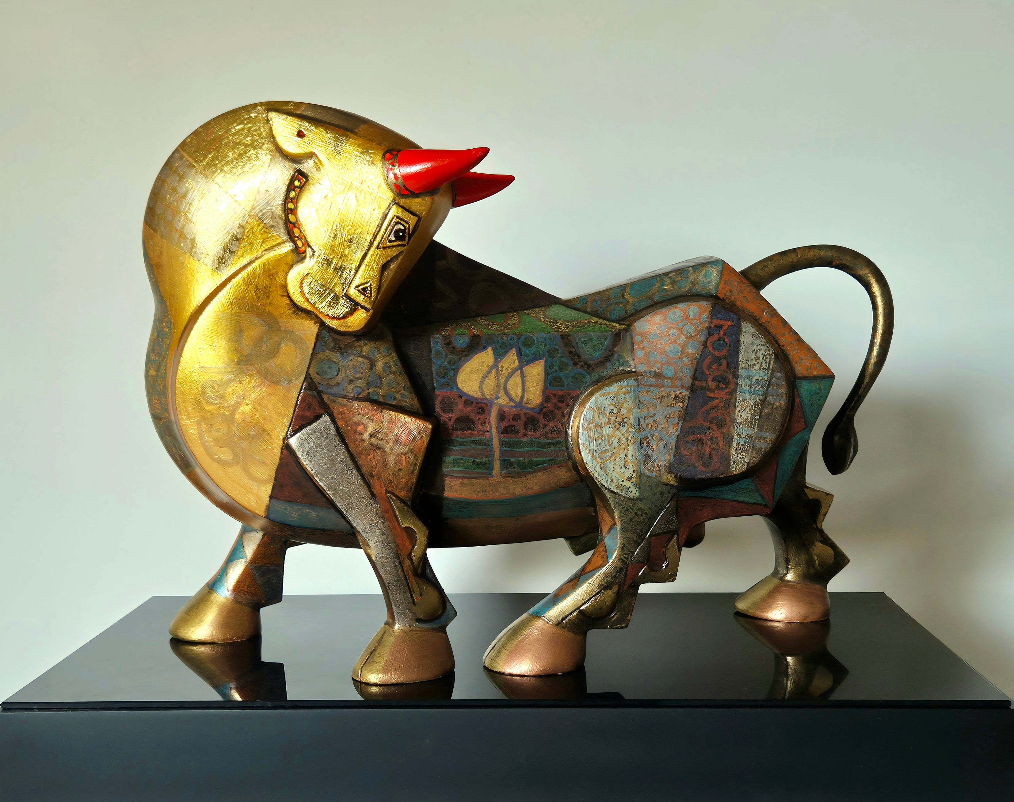 A stylized fiberglass bull sculpture titled 'Celebration' by Dinkar Jadhav, featuring a gold-toned head, red horns, and a body covered in colorful geometric and floral patterns.
