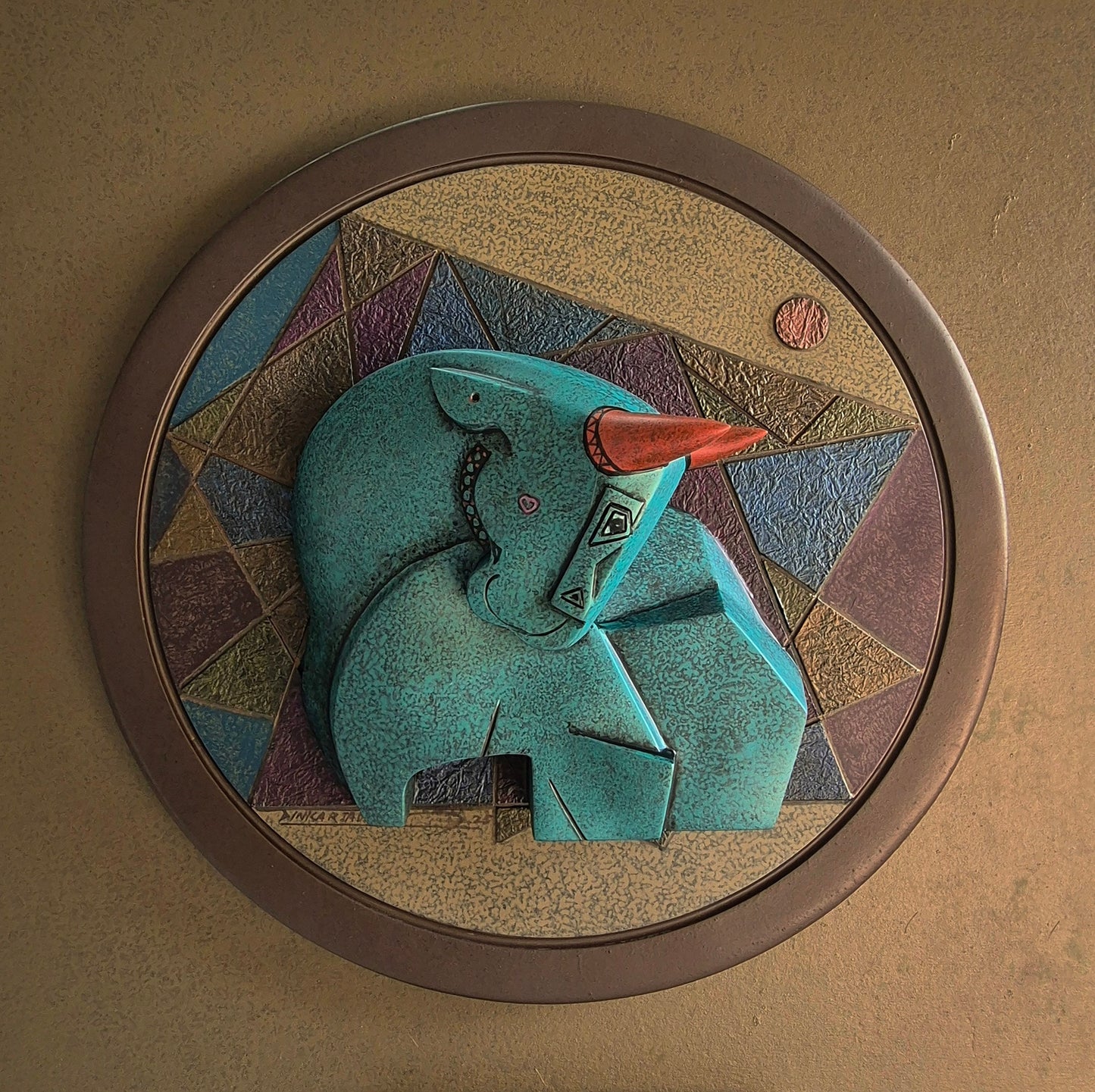 A circular wall-mounted relief sculpture titled 'Celebration' by Dinkar Jadhav, featuring a turquoise-textured stylized bull with red horns against a geometric background.